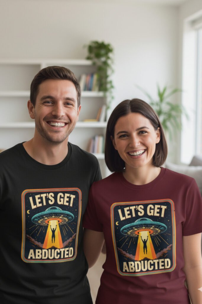 camisetas frikis con humor Pareja joven sonriente con camisetas frikis con humor ‘Let’s Get Abducted’, diseño retro de ovni y abducción en colores vivos