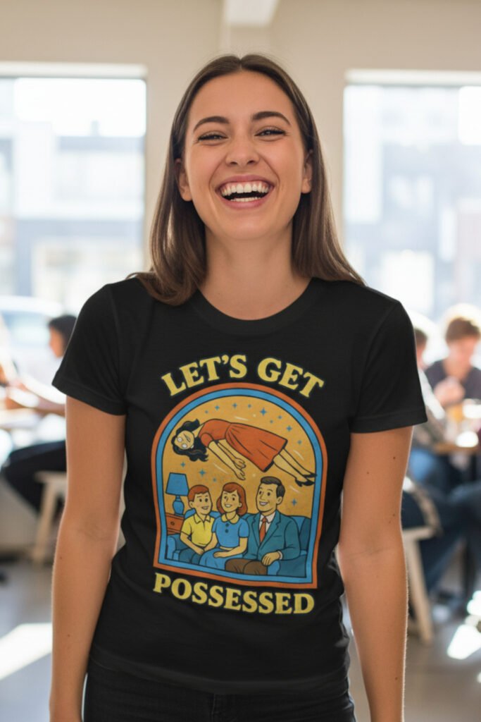Mujer joven sonriente con camiseta negra de estilo retro con diseño humorístico "Let’s Get Possessed" en un ambiente interior luminoso